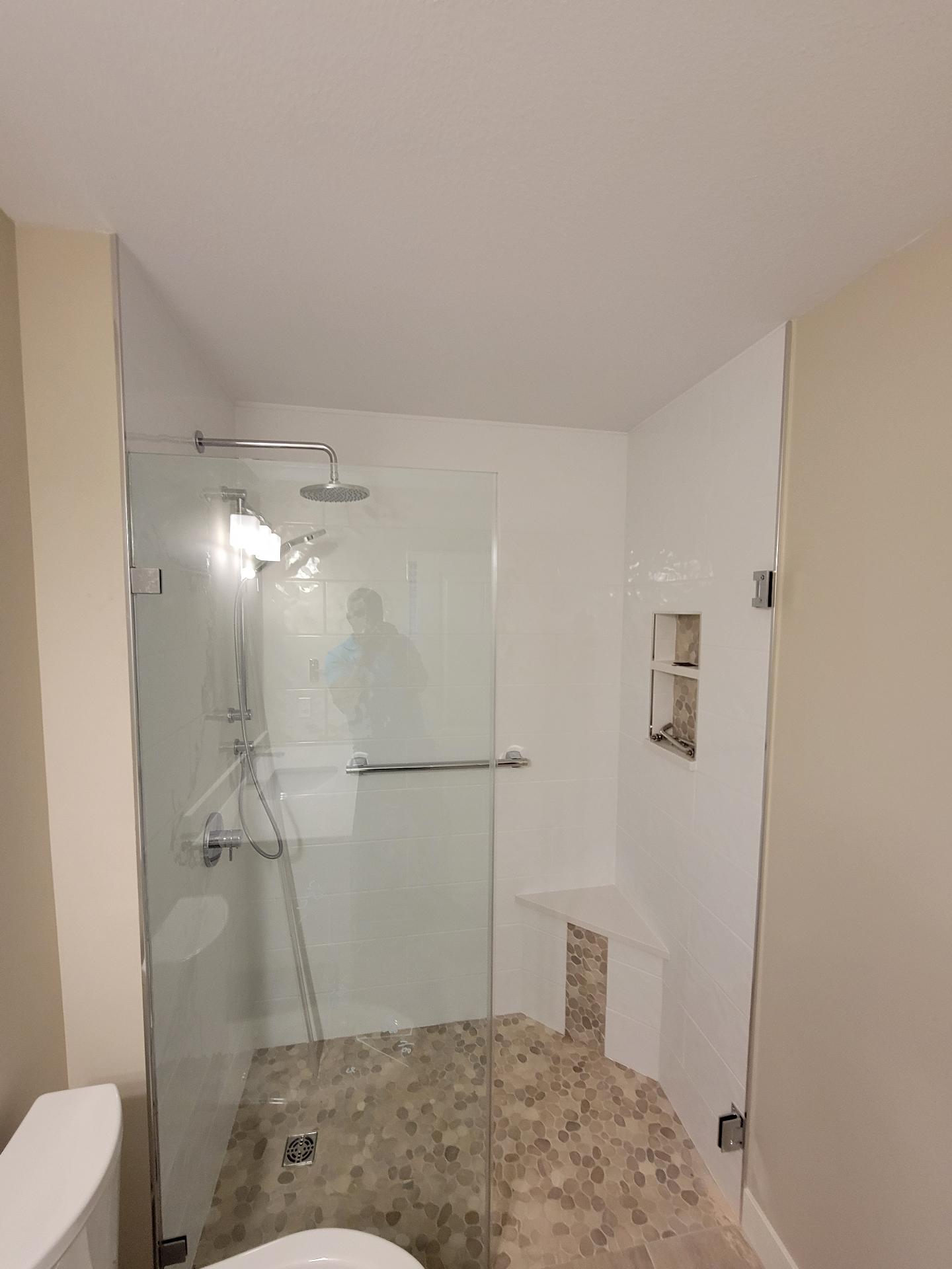 Walk-in shower with rainfall head, pebble floor, and corner bench