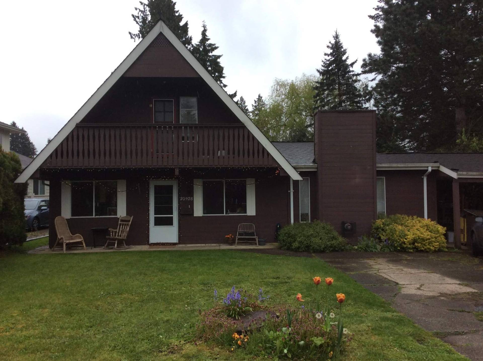Original A-frame home exterior with dark brown siding and worn balcony railing
